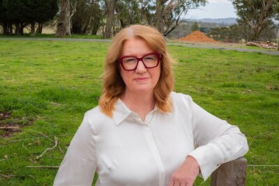 Suzanne Harrison in a white shirt and red glasses in a field 