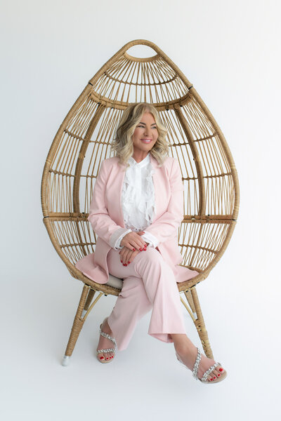 Expert coach dealing with a mid-life crisis, seated on a unique chair and dressed in a stylish pink outfit. This image highlights the personalized and professional support offered to women navigating significant life transitions.