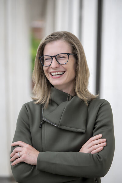 A person in glasses with their arms crossed, smiling 