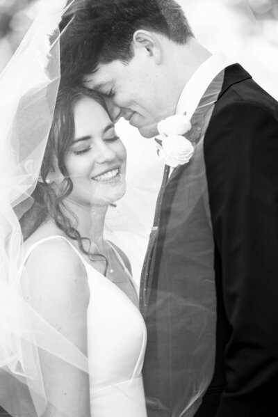 Black and white photograph of bride and groom smiling with heads together under her veil at Freedom Park by Charlotte wedding photographers DeLong Photography
