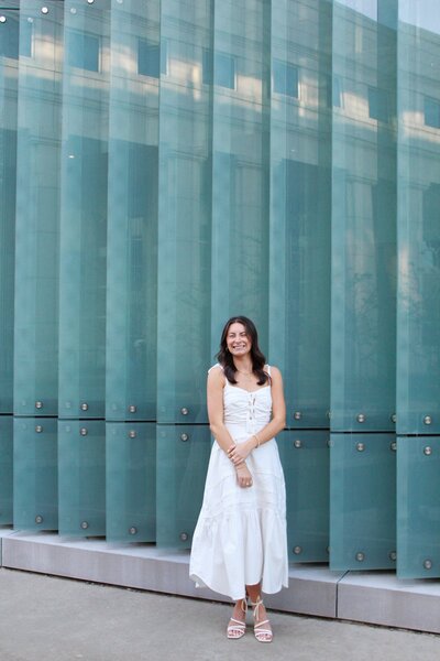 Woman in white dress in front of teal building