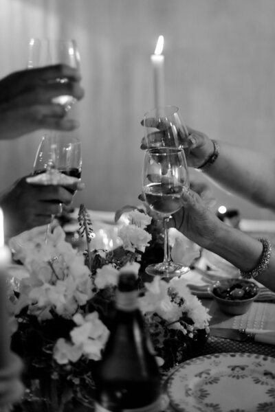 Black and white action shot of wedding guests clinking glasses during a Welcome Dinner at Bastide de Pierres