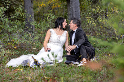 Bride and Groom sitting in the forest on a blanket with champagne and toasting.