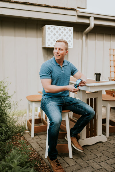 Online dating profile photo of a man sitting confidently on a patio, captured during a relaxed and natural portrait session by Shannon Kathleen Photography in Minneapolis.