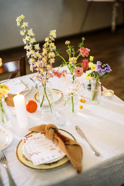 Small vases of florals sat on table with candles and place settings, designed by New Jersey floral designers, Jassamine floral and events.