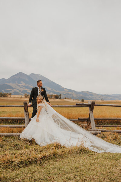 Bride and groom on rustic fence in front of the mountains