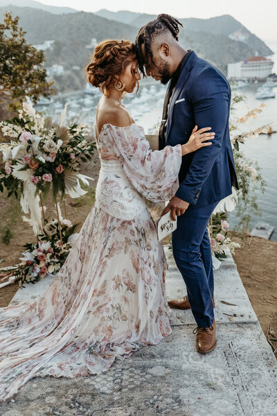 bride in floral gown having a quiet moment with groom in blue suit in catalina island california overlooking avalon harbor