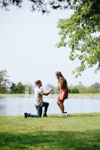 man kneeling to propose to girlfriend by lake