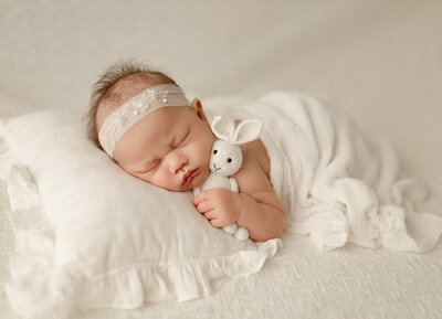 Newborn baby girl peacefully sleeping on a blush backdrop, wrapped in a soft blanket and wearing a delicate headband  - photographed  By Duehr Photography in Maple Grove,MN