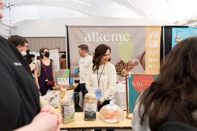 Melinda Kopet speaking with customers at the Alkeme booth during the Gluten Free Expo, demonstrating brand interest and connection.