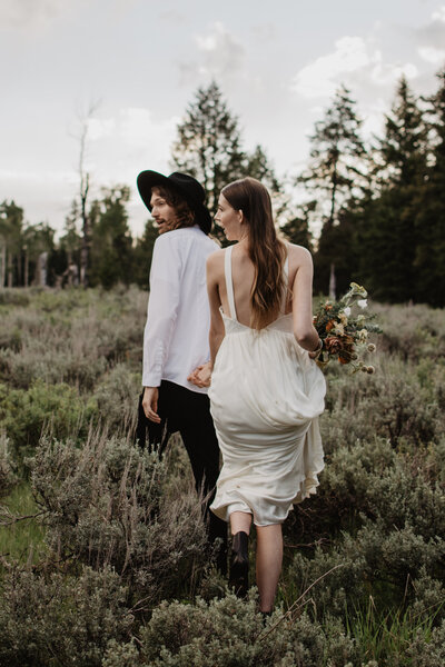jackson hole wedding photos with bride and groom walking through a meadow in the canyon for their wyoming elopement in the summer time