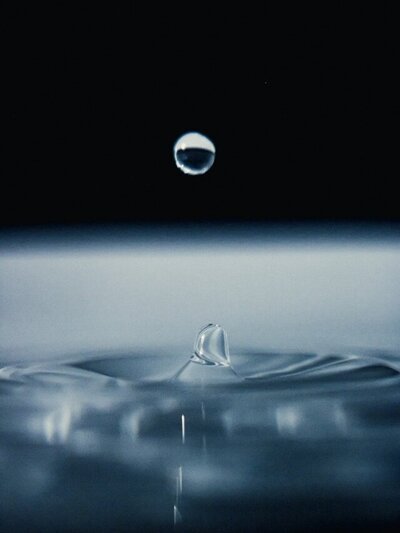 Single droplet creating gentle ripples on a calm water surface.