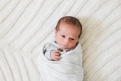 Newborn baby swaddled in a white blanket resting on a textured surface, captured in one of our family photography packages.