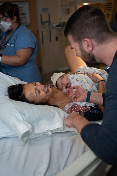 a mother laughs because she can't believe she has just given birth! She is holding her new baby as her husband reaches over to touch the baby's tiny fingers.