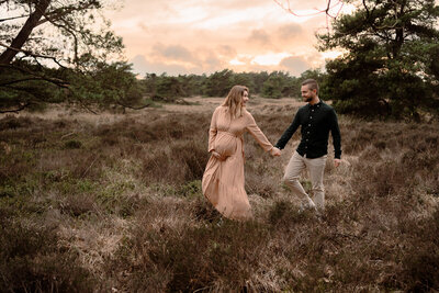 Zwangere vrouw met haar partner lopen door de natuur tijdens een zwangerschapsshoot.