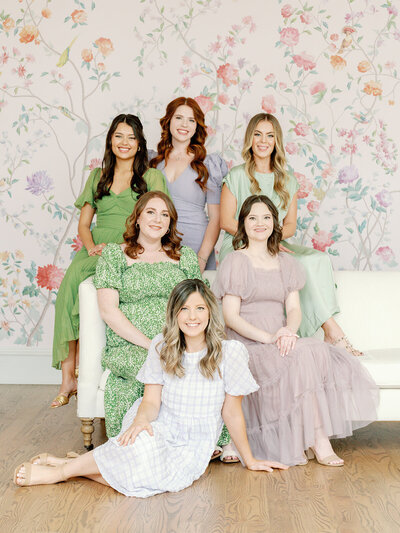 Photo of the Spell Events wedding planning team sitting around a white couch in front of a floral wall