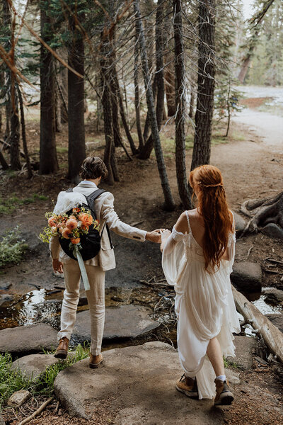 bride and groom hiking through woods crossing a stream