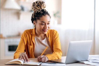 Black woman in a yellow shirt at a desk studying for her PA Exams 