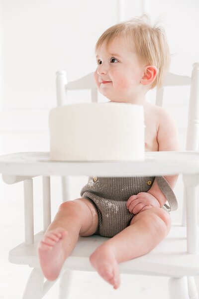 A baby sitting in a high chair with a cake, captured beautifully by Charlotte baby Photographer.