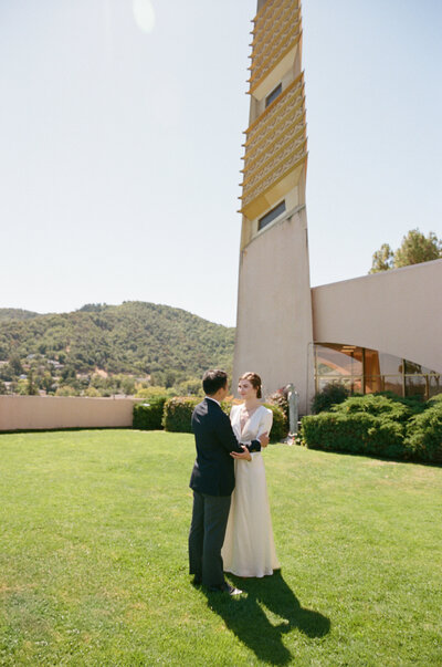 Couple standing on lawn with Civic Center spire in background.