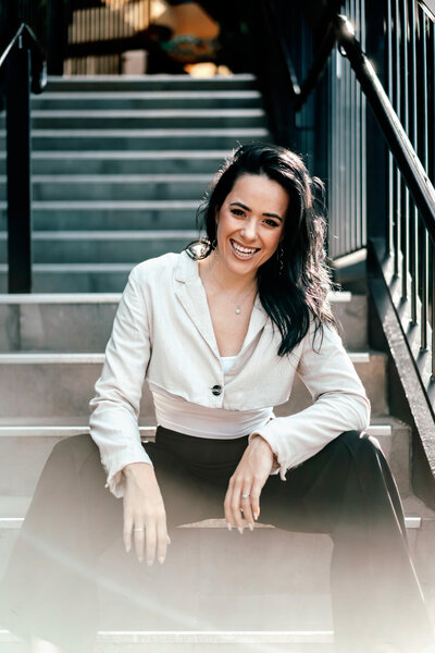 Auckland wedding and proposal photographer Zanthe Vorsatz sitting on stairs, smiling, ready to capture romantic love stories.