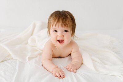 baby laying on white bed by Newborn photographer Boston