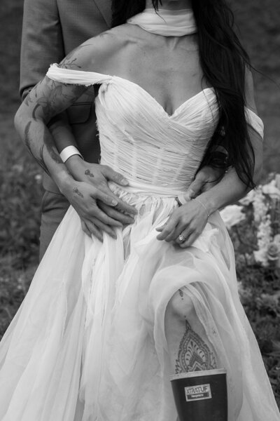 a close up image of a man in a suit standing behind a woman in a wedding gown and holding her waist. 