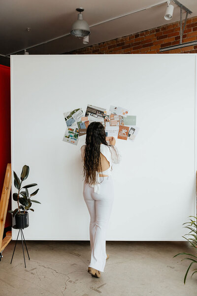 Taysha hanging print outs on a white wall creating a moodboard.