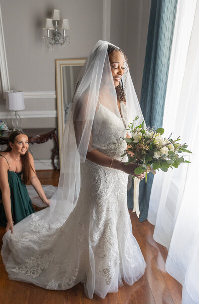 Bride next to window looking down on her bouquet smiling and getting ready for her wedding