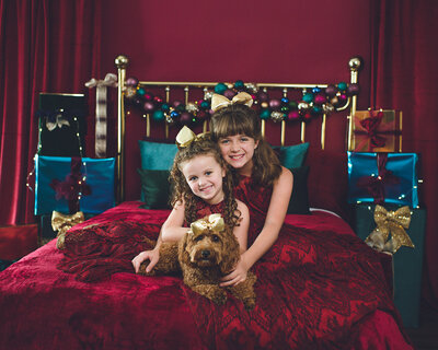 sisters and pet dog in holiday themed bedroom set for mini session pictures