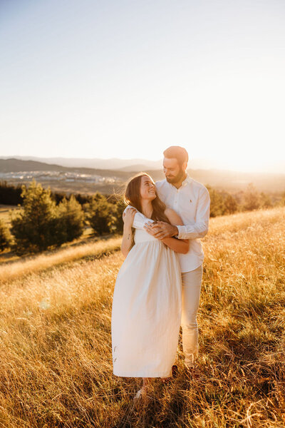 Stnning golden sunset at the National Arboretum Canberra with engaged couple embracing in the foreground. Photo by Acacia & Grace