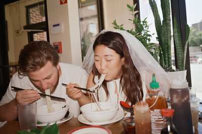 Candid film photo of a bride in a satin gown taking a playful bite of food during her wedding reception — captured by a film wedding photographer at Castillo Holliday Photo + Film.