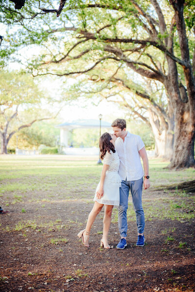 Engaged couple in the park at sunset, with the groom lifting the bride under oak trees with hanging moss