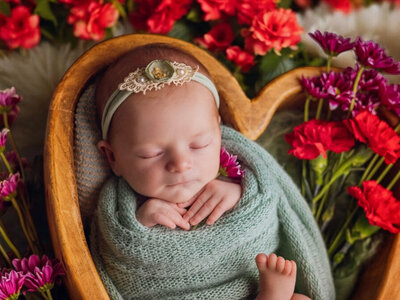 Newborn baby girl nestled in a heart-shaped wooden prop, surrounded by delicate flowers.
