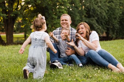 A family with two children playing and laughing together on a grassy lawn, captured beautifully by a Pittsburgh family photographer.