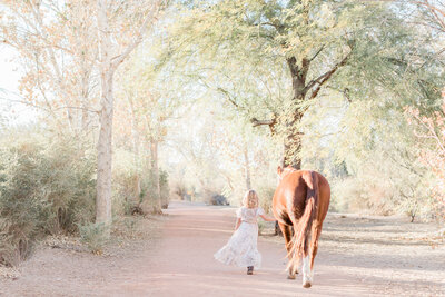 Monterey young girl walking her horse through a path lined with large trees