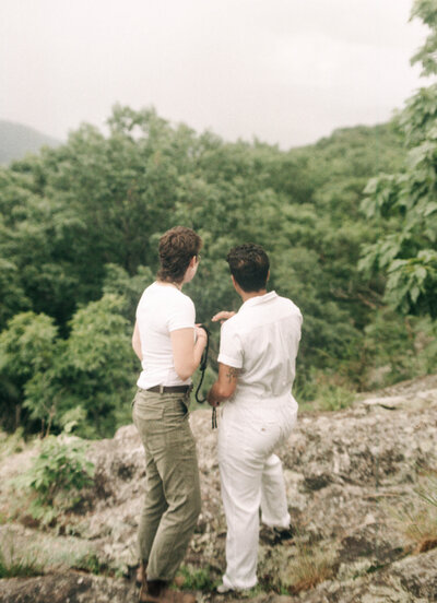 Cinematic wide shot of the couple embracing on the summit, with soft focus and natural light.
