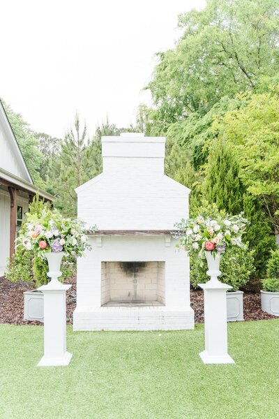 A white brick fireplace on the lawn with flower vases on both sides.