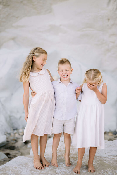 Three children posing for a photo in front of a white rock in Pismo Beach 