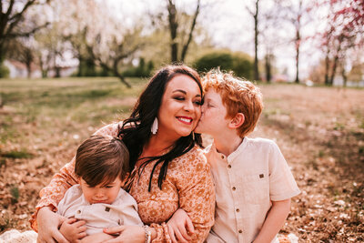 mother and sons sitting little boy kissing moms cheek Missouri spring