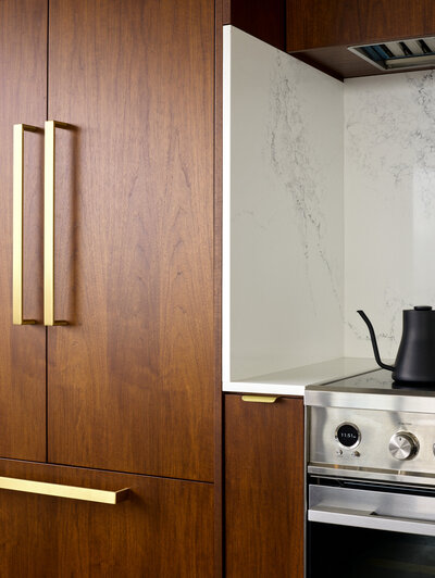 Walnut cabinetry with gold accents next to a stainless steel stove range with an elegant white marble backsplash.