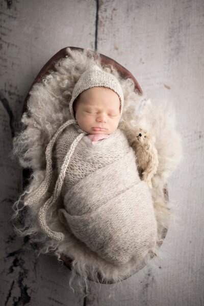 Newborn with teddy sleeping  in neutral wrap and bonnet in studio photography