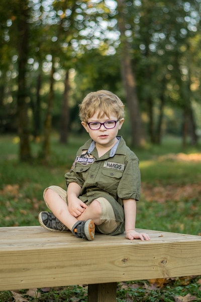 A young boy sits on a bench in the woods.