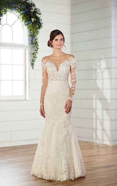 WEDDING DRESS WITH LACE SLEEVES AND V-NECK A gown that brings all the romance to any wedding day, this wedding dress with lace sleeves and V-neckline from Essense of Australia is simply breathtaking! Soft, cotton lace covers the bodice of this gown, giving a modern update with its unique, floral lace pattern. A deep V-neckline is the focal point of the bodice, extending easily into an off-the-shoulder neckline that has an organic lace edge. This romantic lace detailing carries down the arms, providing a good amount of coverage to the entire arm. From the waist down, the fitted skirt of this dress shows off your curves effortlessly before flaring out at the knees. The back of the gown is open and is highlighted with sheer, illusion-lace details and organic lace detailing throughout the skirt and train. The back of this wedding dress with lace sleeves and V-neckline zips up beneath crystal buttons.