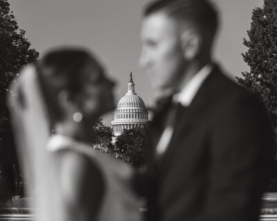 Black and white photo with bride and groom out of focus and the US Capitol Building