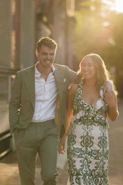 Romantic engagement photo of a couple during golden hour in Old City Philadelphia, with the groom wearing a muted sage green suit, capturing timeless elegance in warm, soft light.