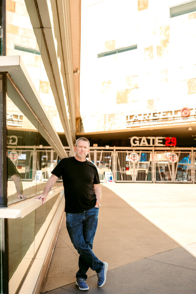 Professional dating profile photo of Kerry walking confidently downtown Minneapolis under a theater marquee, dressed casually in jeans and a black shirt.