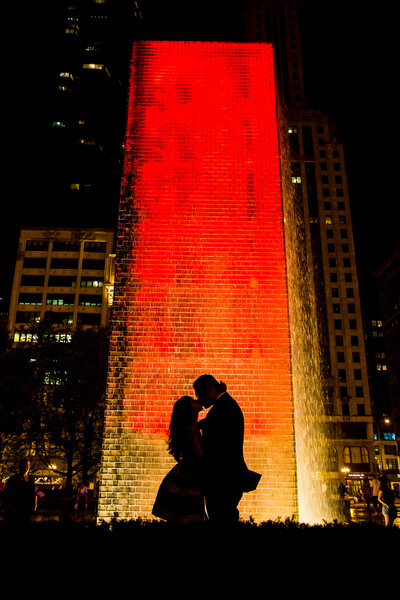 A silhouette image at night  of an engaged couple kiss in front of a fountain in downtown Chicago.