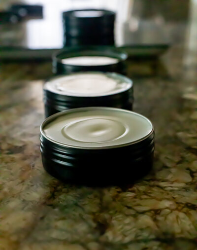 Multiple rosemary honey body balms in tin canisters laid out in a row on the counter