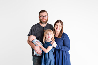 A family of four smiling at the camera during a newborn photo session at a studio  in Huntsville